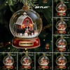 Christmas ornament with a barn and cows inside a snow globe, displayed on a tree.