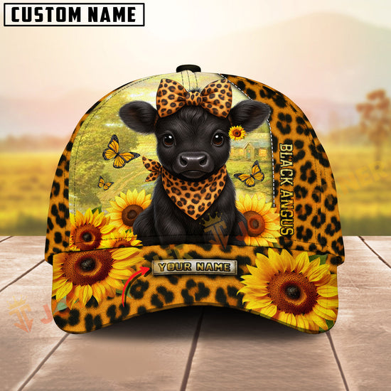 Cap with a black Angus cow design, sunflowers, and butterflies on a wooden surface with a blurred natural background.