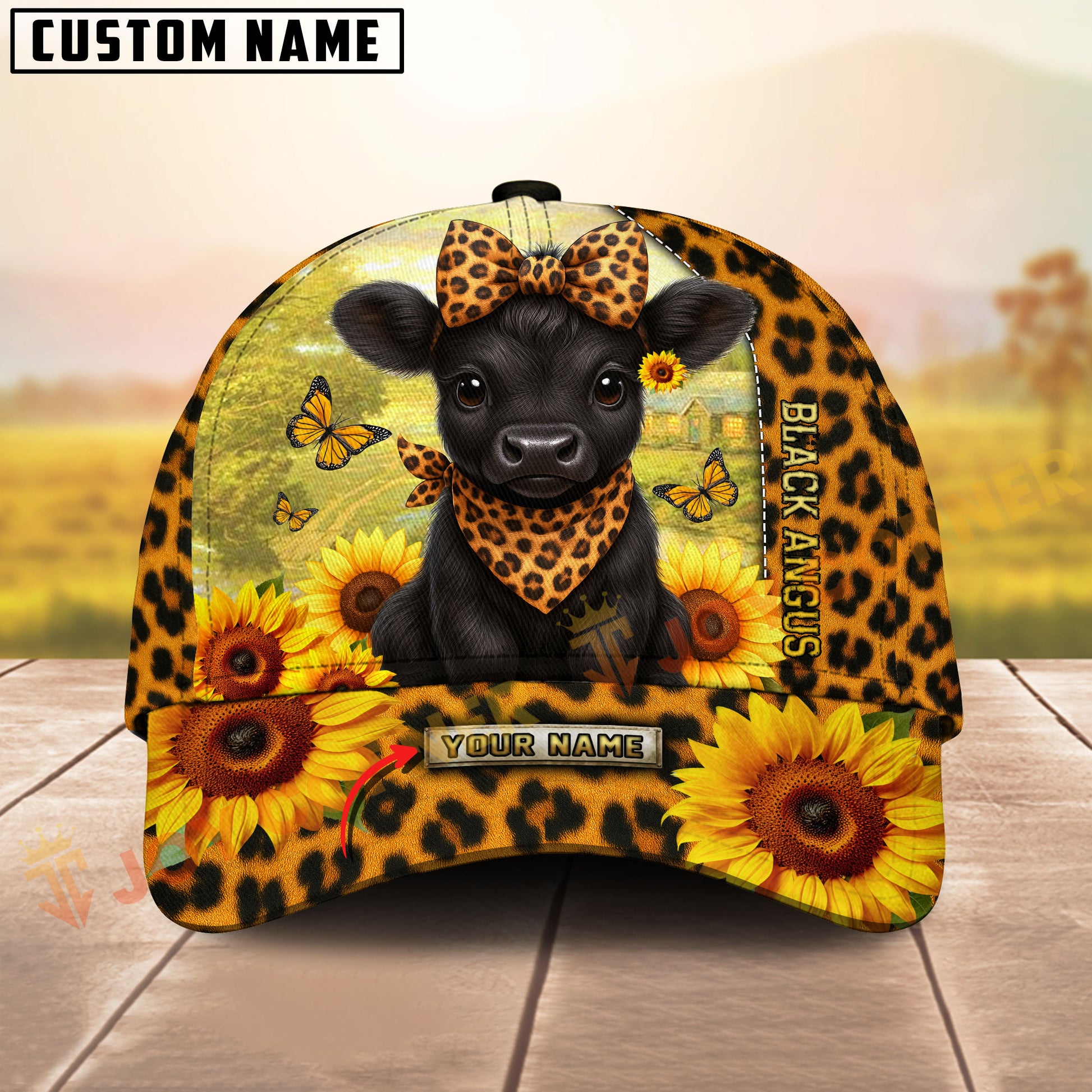 Cap with a black Angus cow design, sunflowers, and butterflies on a wooden surface with a blurred natural background.