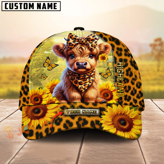 Cap with Highland cow design, sunflowers, and butterflies on a wooden surface with a blurred natural background.