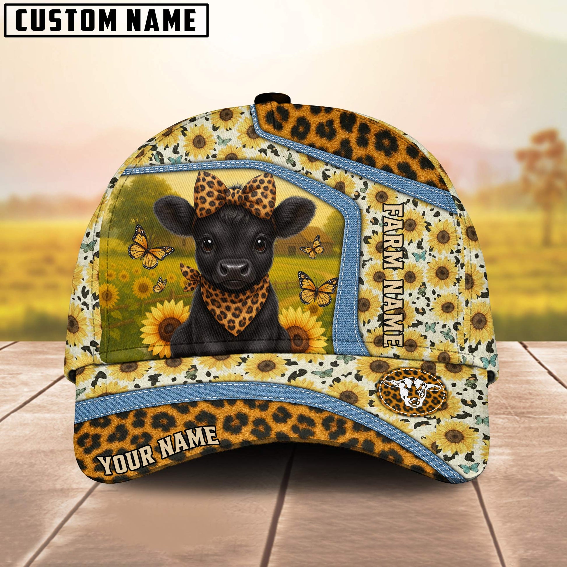 Cap with a black cow design, sunflowers, and butterflies on a wooden surface with a blurred natural background.